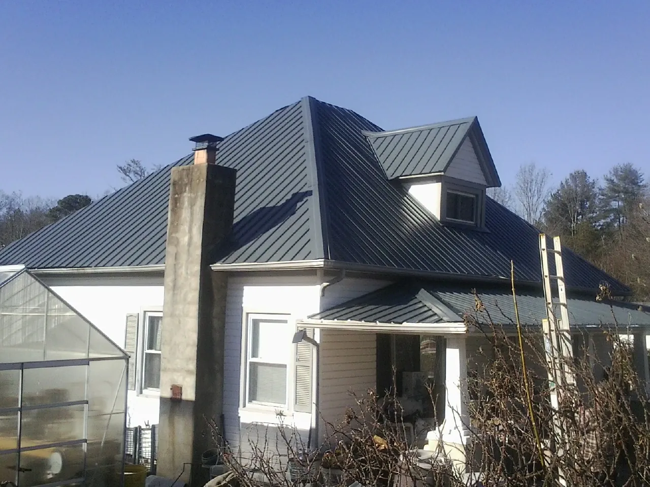 Dark blue standing seam metal roof on a white farmhouse with dormer — Slate & Tile Roof Repair by Roofing Brothers in Jadwin