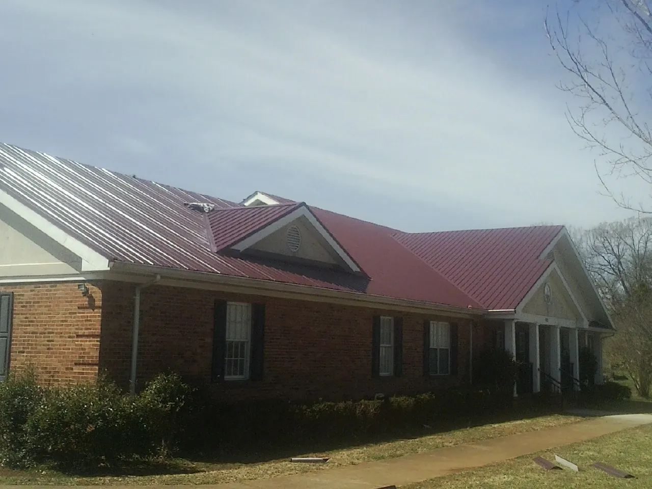 Red metal roof with gabled entries on a long brick building, from a Hail Damage Roof Repair job in Jadwin