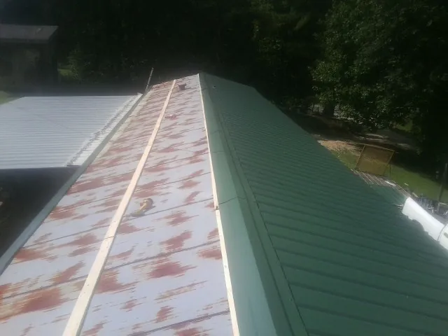 Old rusted panels beside newly installed green metal roofing — Wind Damage Roof Repair by Roofing Brothers in Jadwin