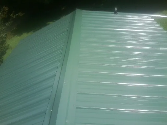 New green metal panels meeting at the ridge of a roof — Flat Roof Repair work by our crew in Jadwin