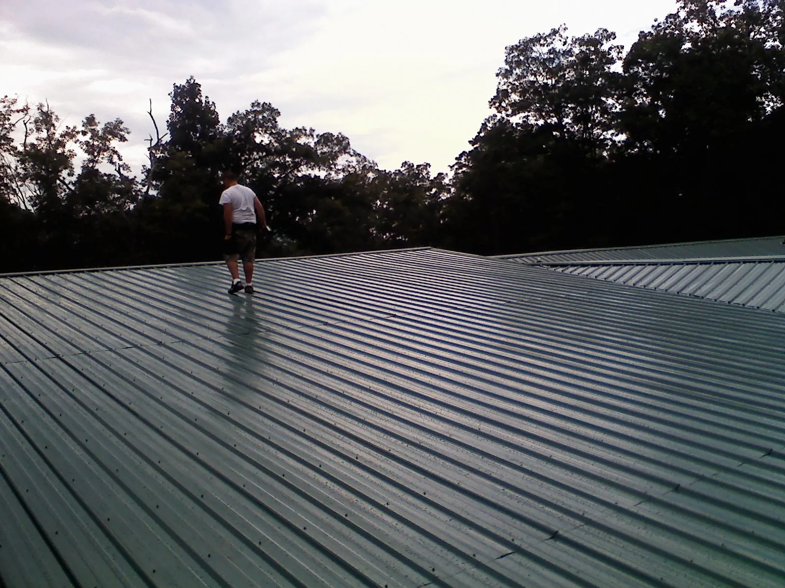 Roofer walking a wide expanse of new green metal roofing in Jadwin